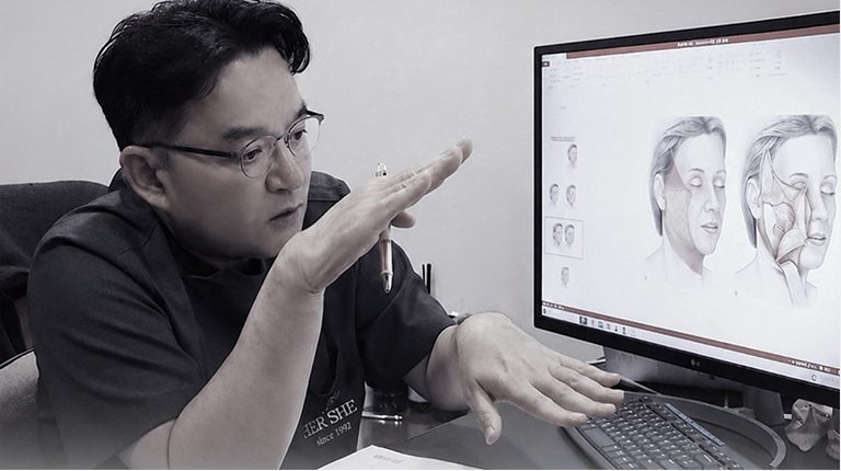 흑백 — 모니터의 안면 해부 그림 앞에서 손으로 설명하는 안경 쓴 의사(1:1 상담)